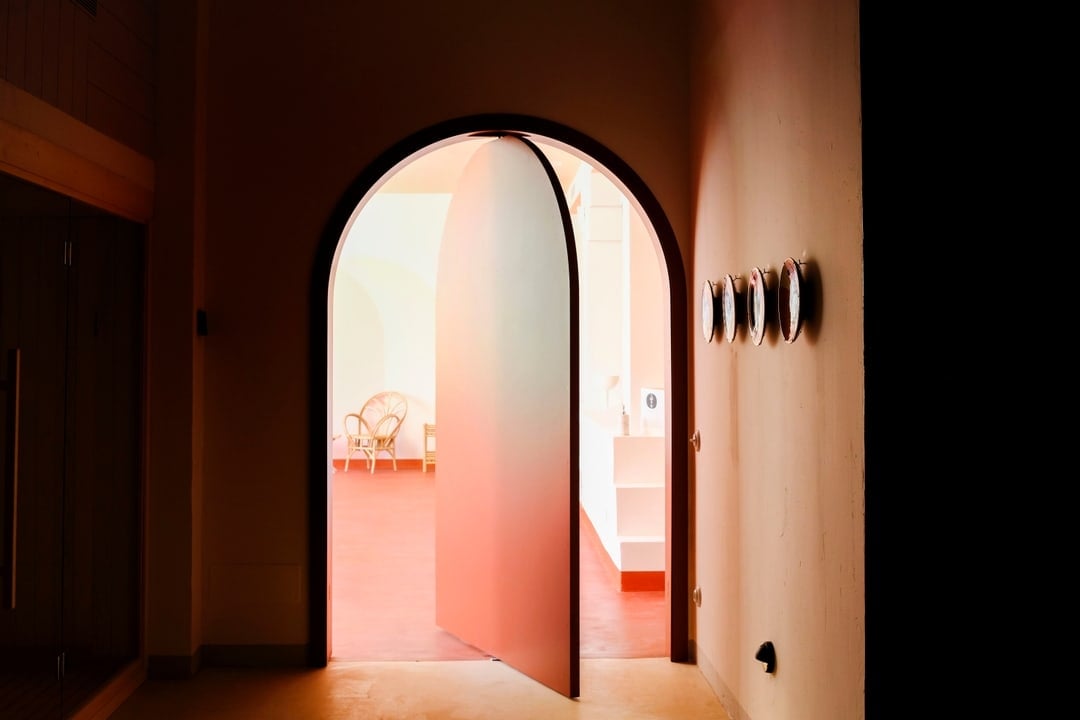Menorca Experimental, Balearic Islands, Spain — Arched doorway with warm terracotta walls framing minimalist interior with natural light and rattan chair.