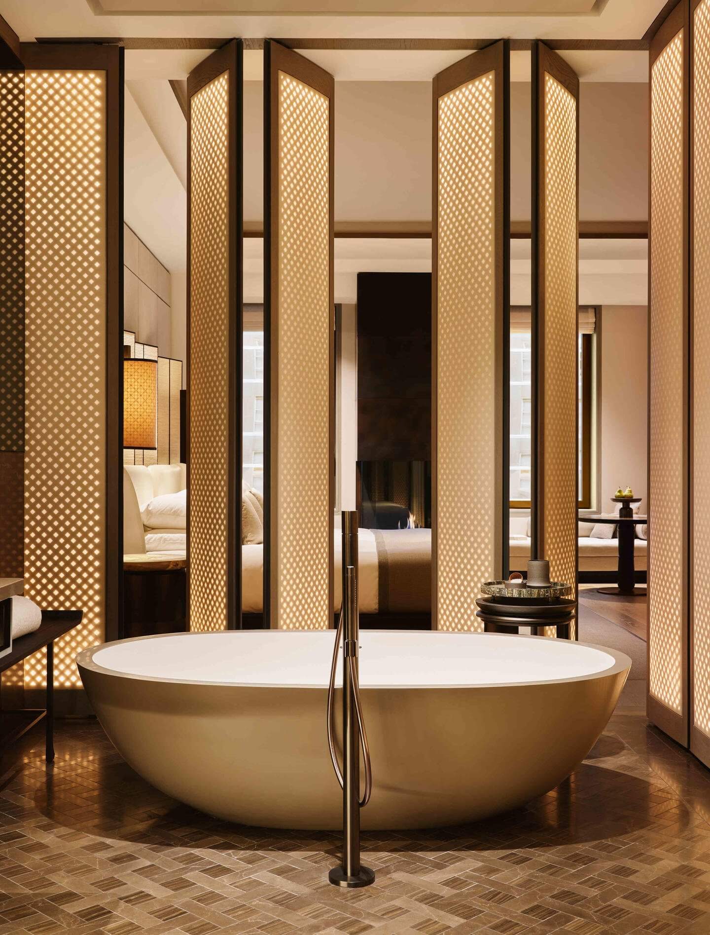 Aman New York, New York, United States — Spa bathroom with sculptural stone soaking tub, latticed wood screens, warm ambient lighting, and herringbone marble flooring.