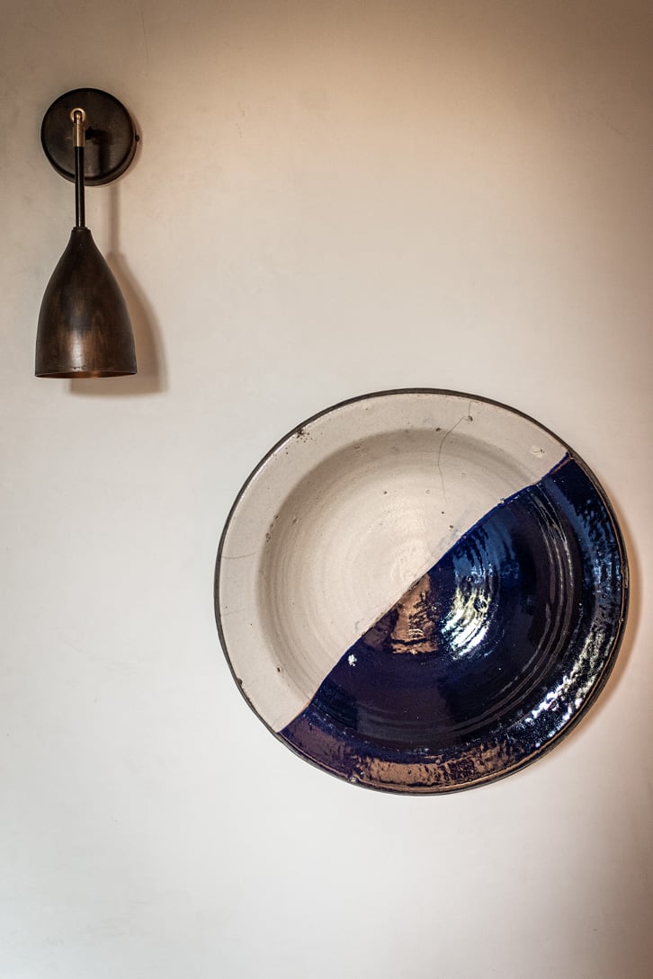 Dimora delle Balze, Europe — Handcrafted ceramic bowl with cobalt blue glaze and natural rim beside bronze pendant light on cream wall.