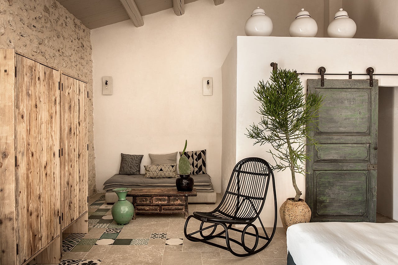 Dimora delle Balze, Europe — Rustic bathroom with stone walls, woven rocking chair, vintage wooden doors, potted plant, and patterned tile floor.