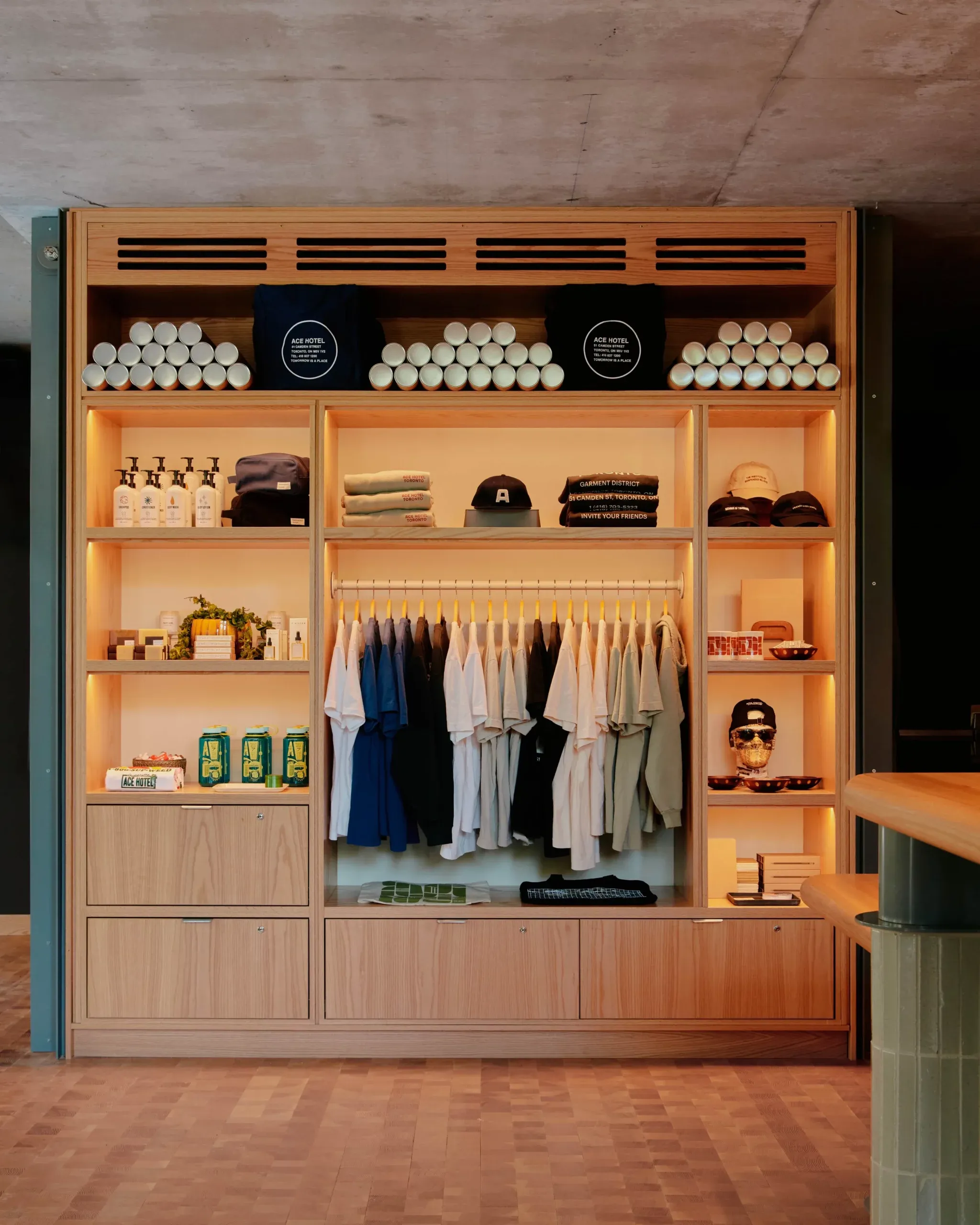 Ace Hotel Toronto, Canada — Wooden display cabinet with warm lighting showcasing apparel, candles, and hospitality merchandise in organized shelving.