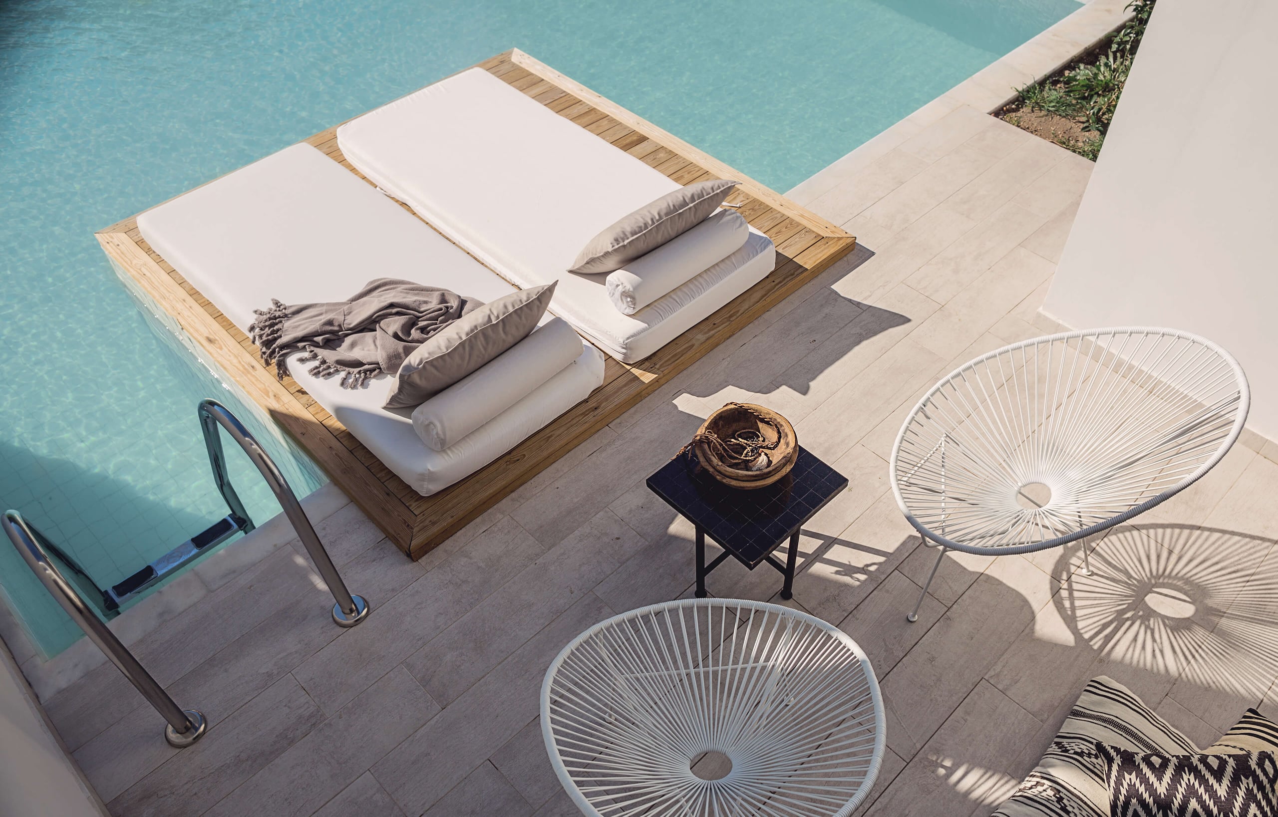 Casa Cook Rhodes, Europe — Sunlit poolside terrace with wooden sunbeds, white acapulco chairs, and turquoise water, minimal luxury resort design.