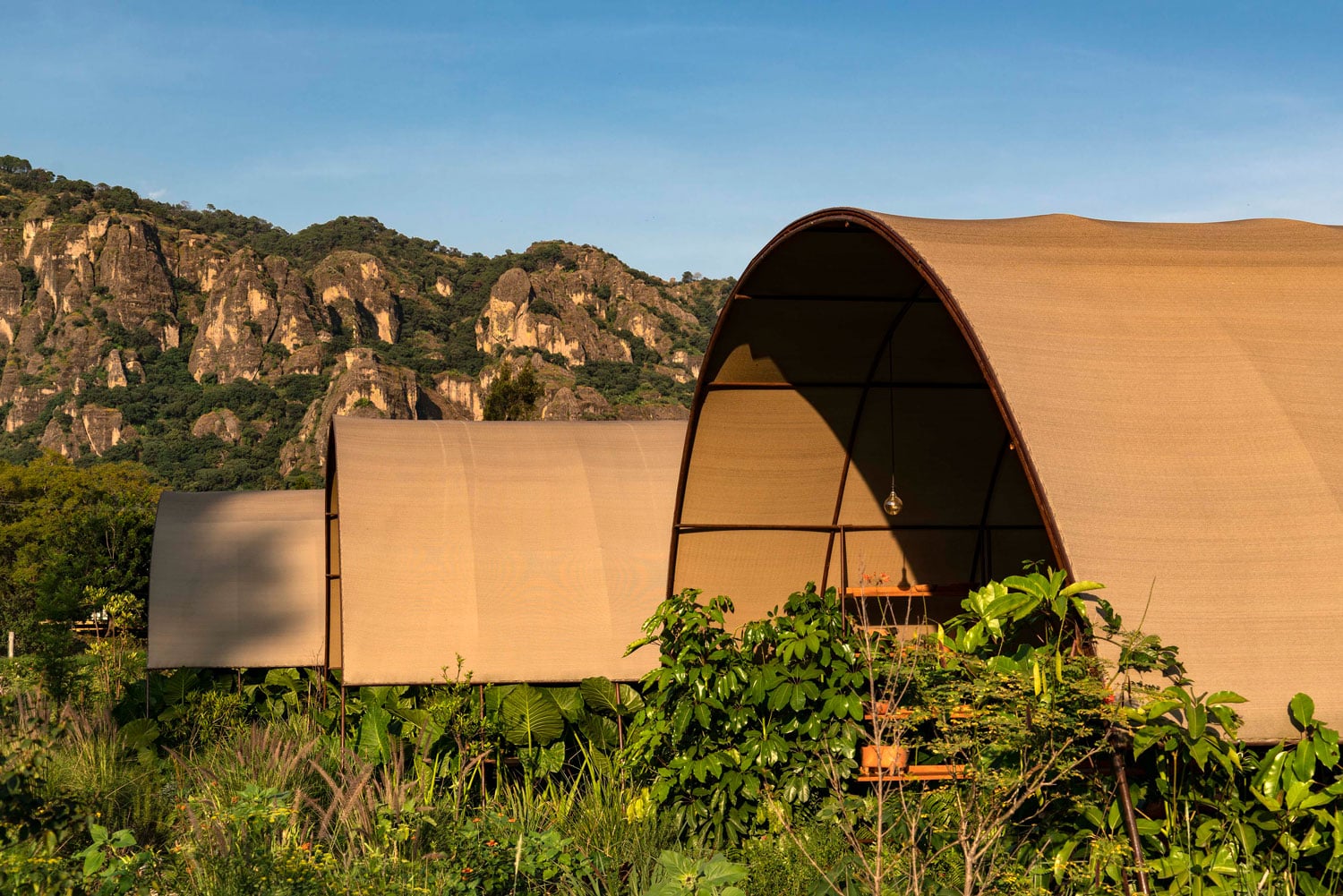 Parcela Restaurante, Mexico — Canvas glamping structure with arched roof overlooking limestone cliffs and lush vegetation in natural light.