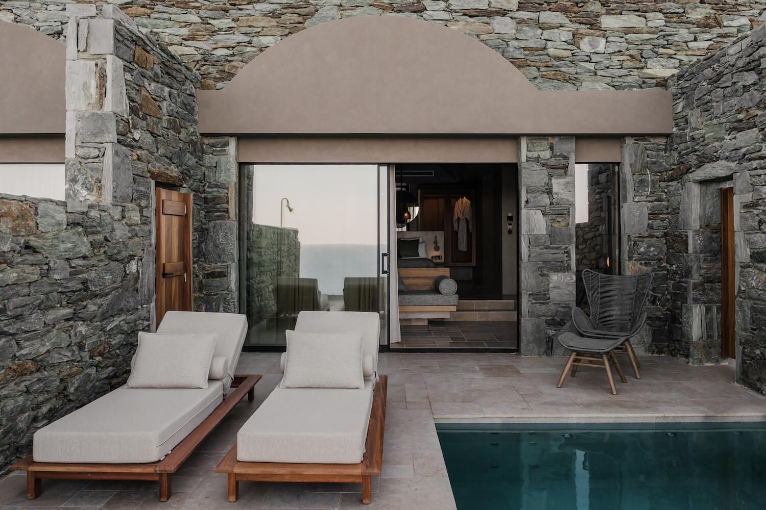 ACRO Suites, Europe — Stone terrace with teak loungers, pool edge, modern glass doors opening to minimalist interior, mountain vista at dusk.