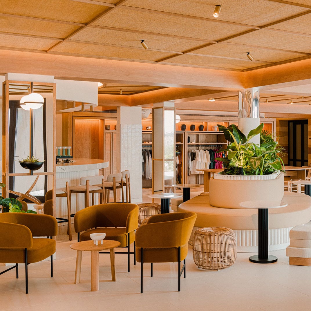 Aethos Ericeira, Europe — Warm wooden ceiling and natural light illuminate a luxury retail space with ochre seating, white planters, and minimalist hospitality design.