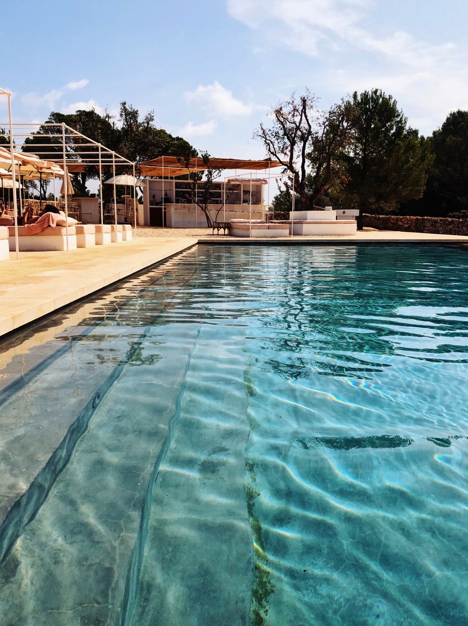 Menorca Experimental, Balearic Islands — Minimalist poolside terrace with crystal-clear water, limestone decking, modernist architecture, and Mediterranean landscape under bright daylight.