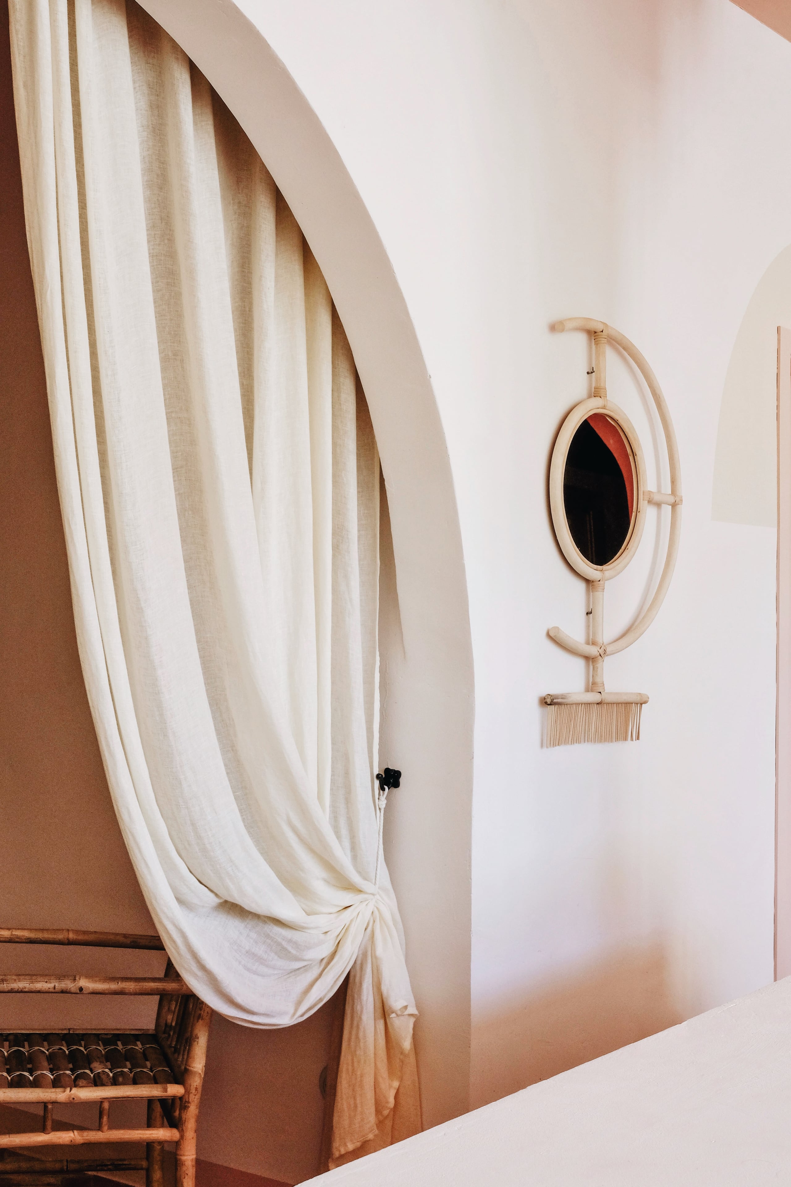 Menorca Experimental, Balearic Islands, Spain — Minimalist interior with draped cream linen curtain, wooden mirror with black glass, and terracotta wall detail in natural light.