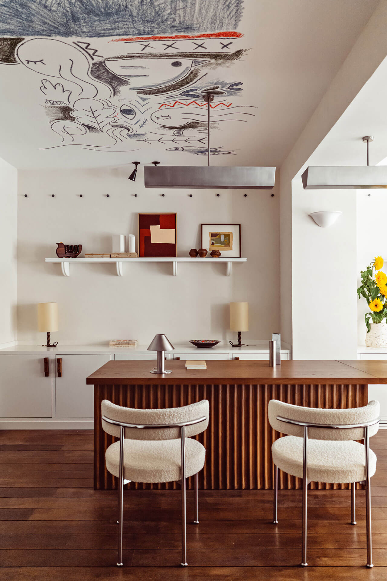 Académies et des Arts, Europe — Modern kitchen with walnut island, cream chairs, white cabinetry, and abstract ceiling mural in charcoal and red.