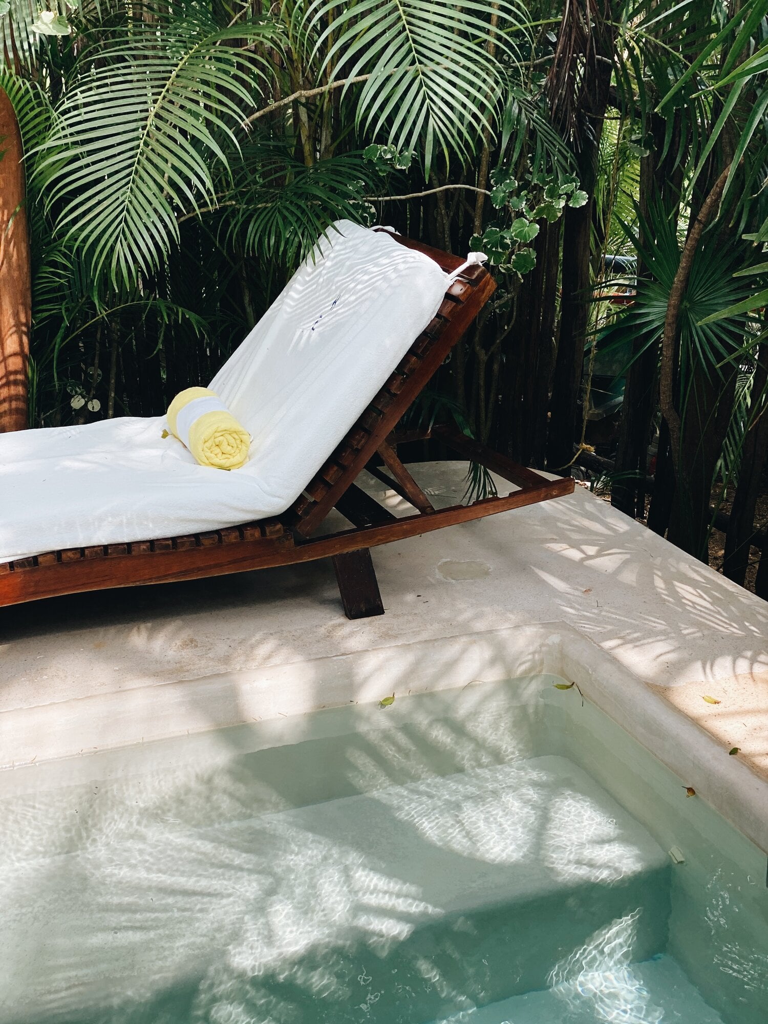 Hotel Esencia, Mexico — Wooden daybed with white linens beside turquoise plunge pool, surrounded by tropical palm fronds and dappled sunlight in secluded garden setting.