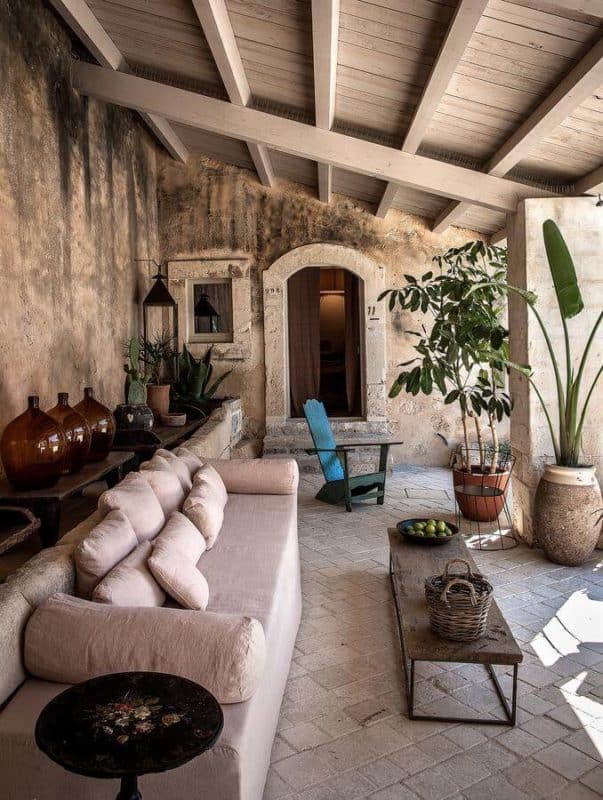 Dimora delle Balze, Europe — Covered terrace with arched doorway, cream linen seating, exposed stone walls, timber ceiling, potted plants, and natural light.