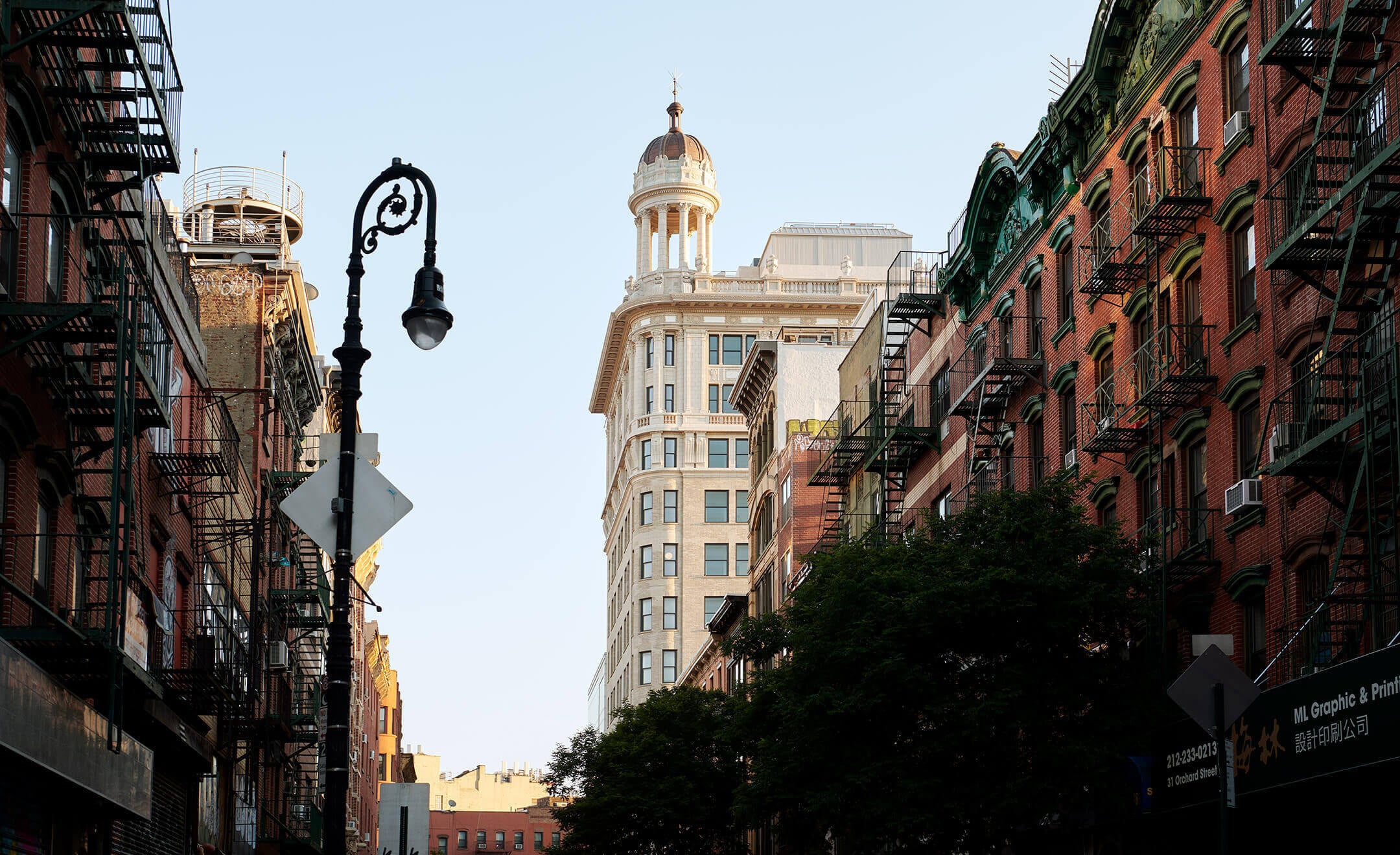 Nine Orchard, New York, USA — Cast-iron street lamp and ornate building dome framed by red-brick facades with fire escapes in historic Lower East Side streetscape.