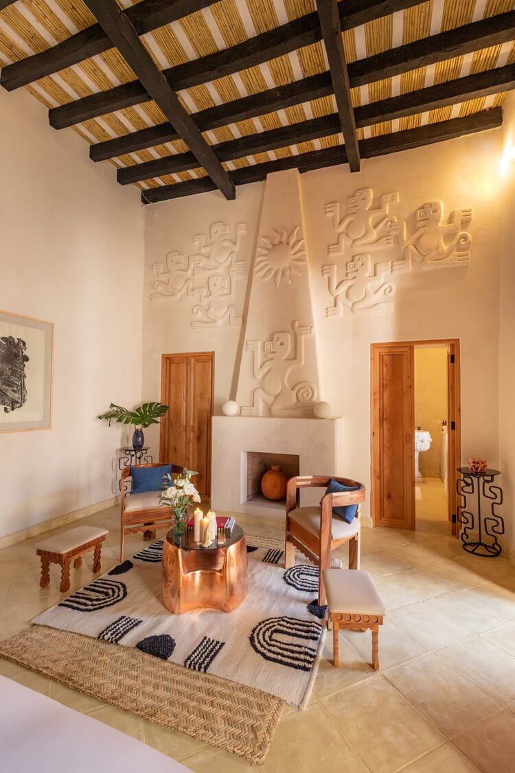 La Valise San Miguel, Mexico — Cream plaster fireplace with carved relief panels, wooden beam ceiling, terracotta vessels, woven rugs, minimalist seating arrangement, warm ambient lighting.
