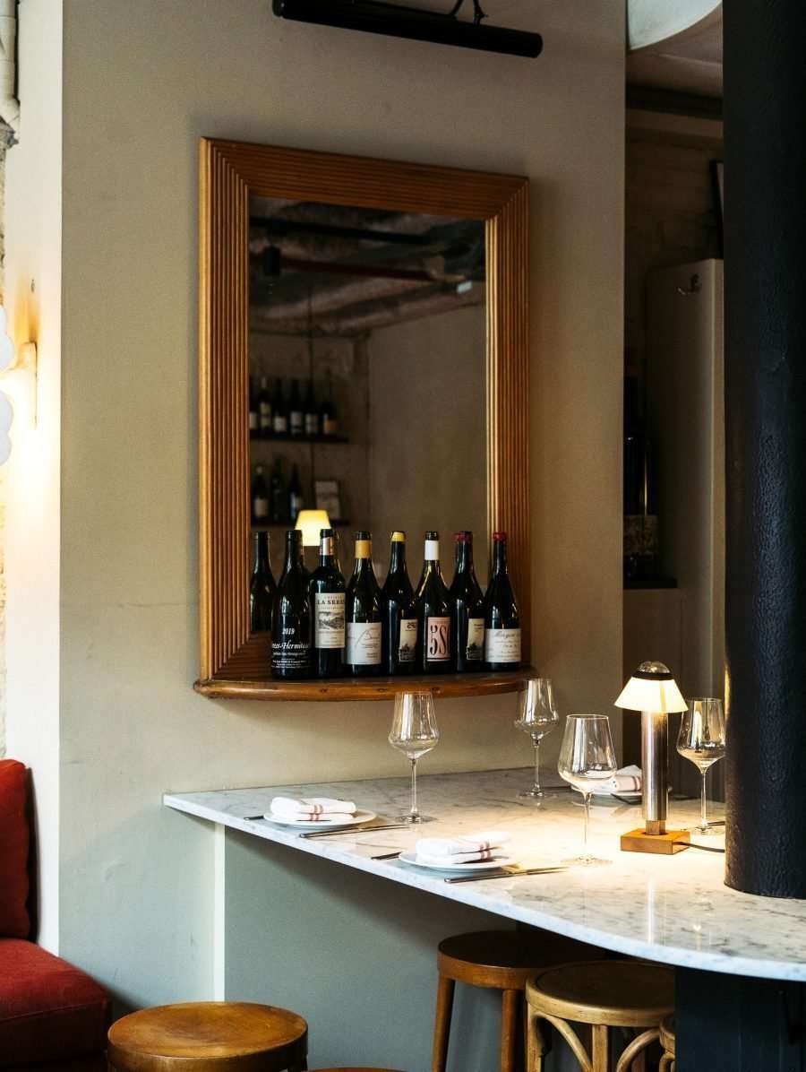 Casa Bonay, Europe — Marble bar counter with wine bottles displayed in framed mirror, wine glasses, and brass lamp lighting contemporary hospitality interior.