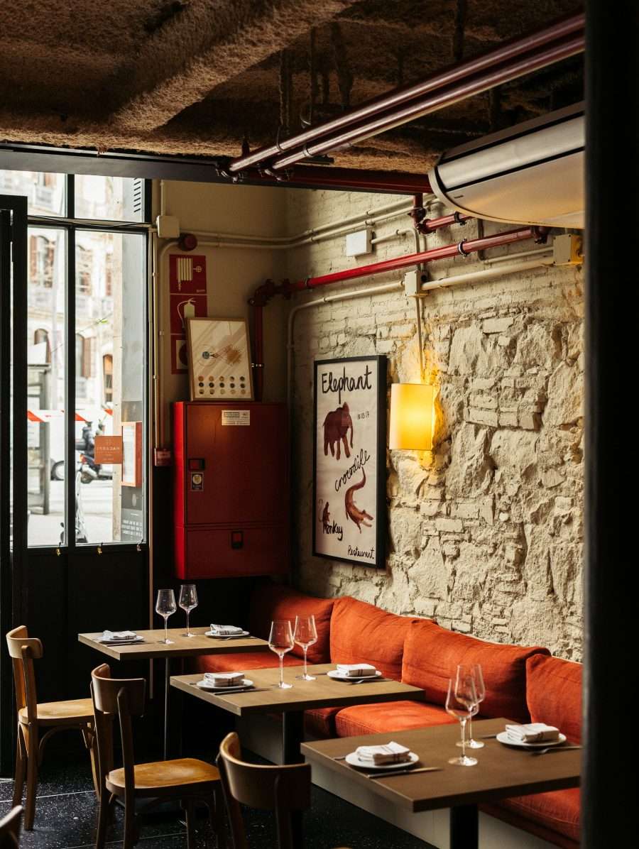 Bodega Bonay, Europe — Intimate restaurant with exposed brick walls, copper pipes, orange banquette seating, and warm ambient lighting creating industrial-modern European dining atmosphere.
