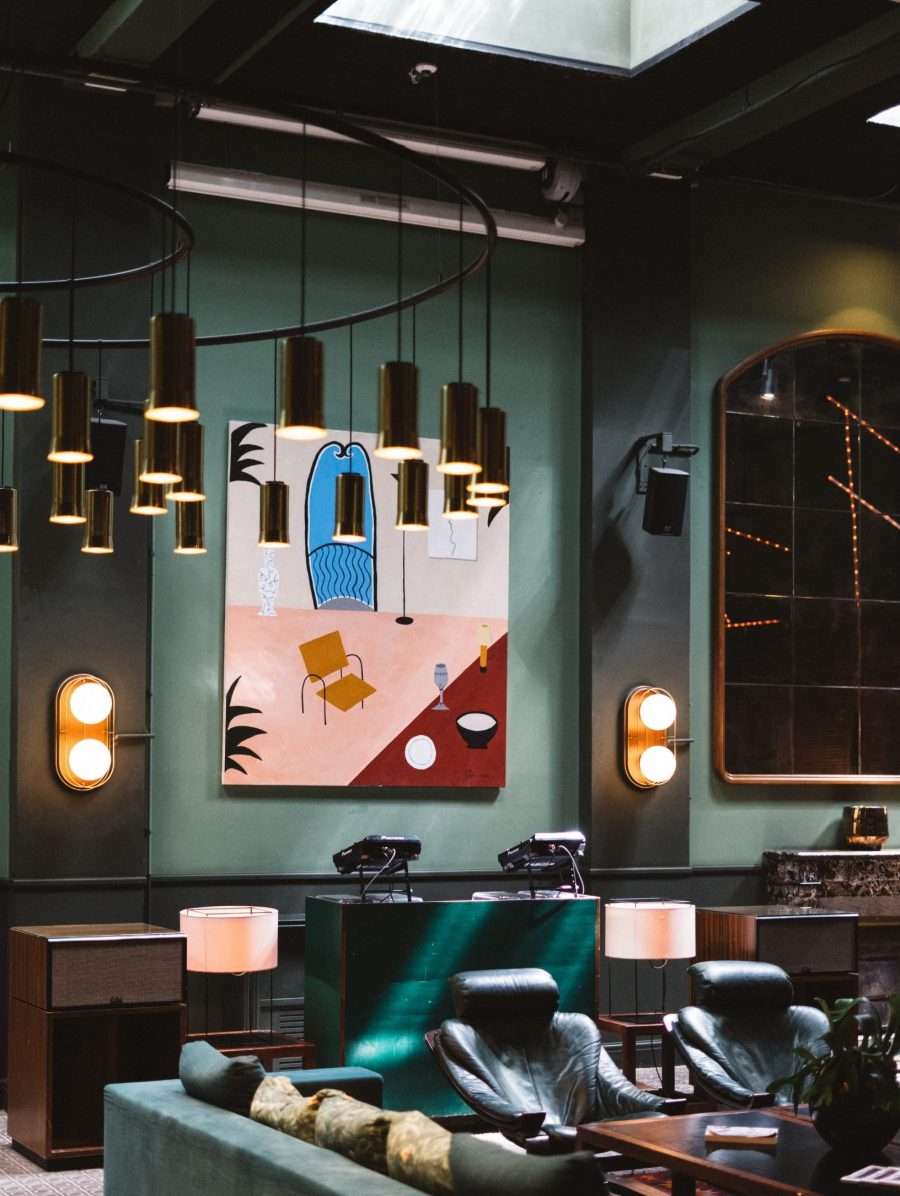 Casa Bonay, Europe — Teal-walled lounge with brass pendant lights, mid-century seating, and contemporary artwork above gas cooktop.