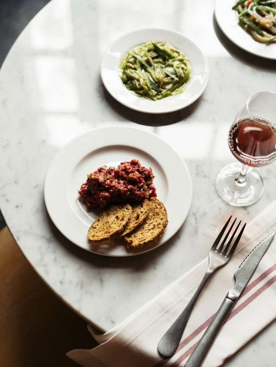 Casa Bonay, Europe — Marble table set with cured meat tartare, toasted bread, pesto pasta, and red wine in minimalist fine dining presentation.