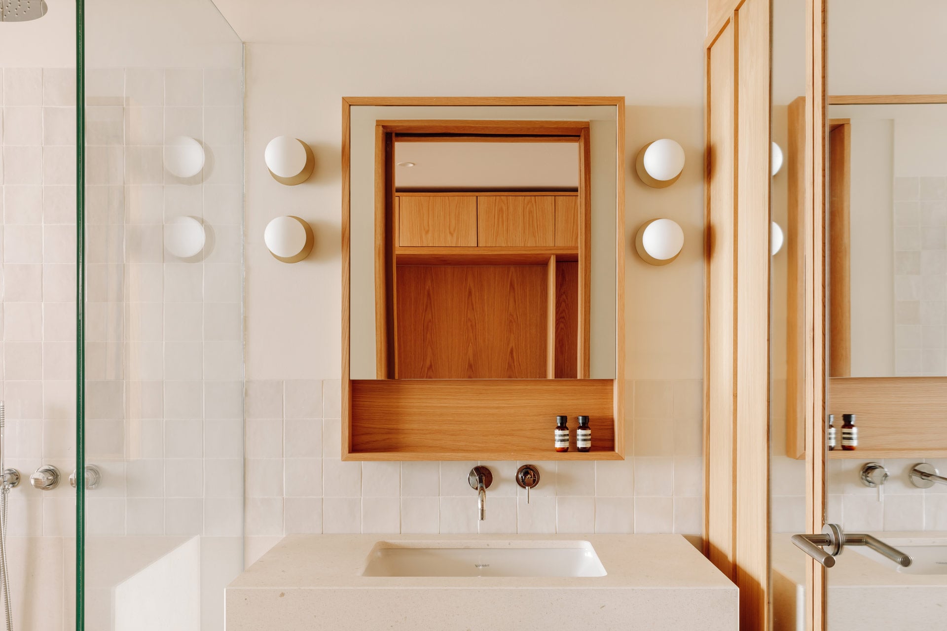 Aethos Ericeira, Portugal — Minimalist bathroom with teak medicine cabinet, marble countertop, white subway tile wall, and brass sconces.