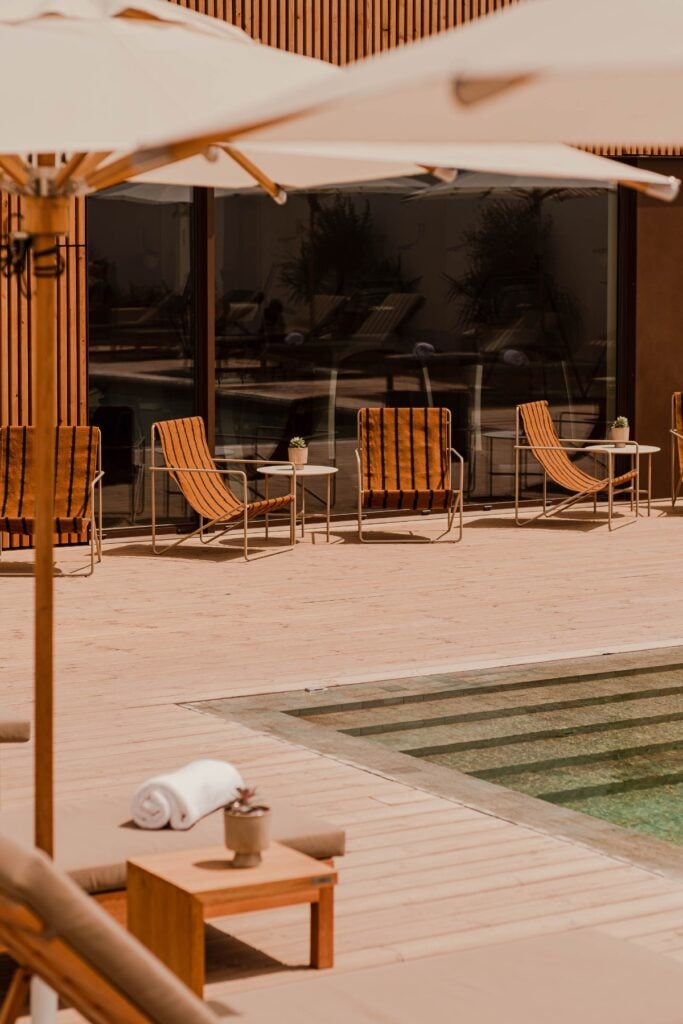 Aethos Spa, Europe — Wooden deck with striped loungers, umbrellas, and minimalist furniture overlooking pool and spa facilities in warm sunlight.