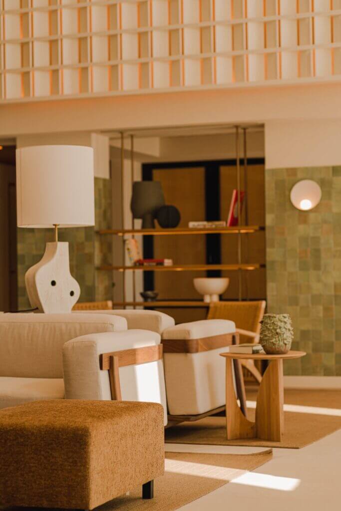 Aethos Ericeira, Portugal — Minimalist lobby with curved caramel upholstery, wooden shelving, sage tilework, and natural light casting geometric shadows.