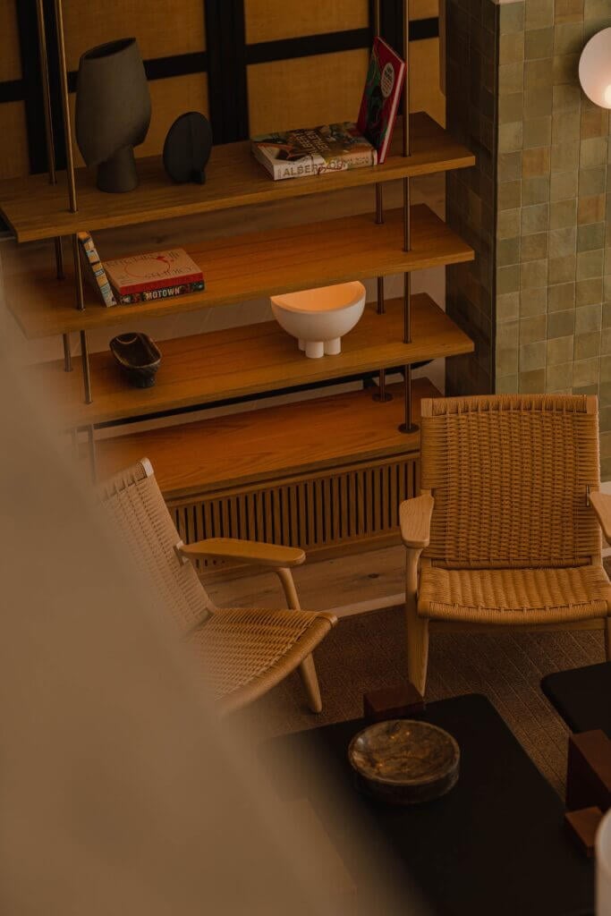 Aethos Ericeira, Portugal — Mid-century woven chairs and tiered wooden shelving with ceramics and books in minimalist interior space.