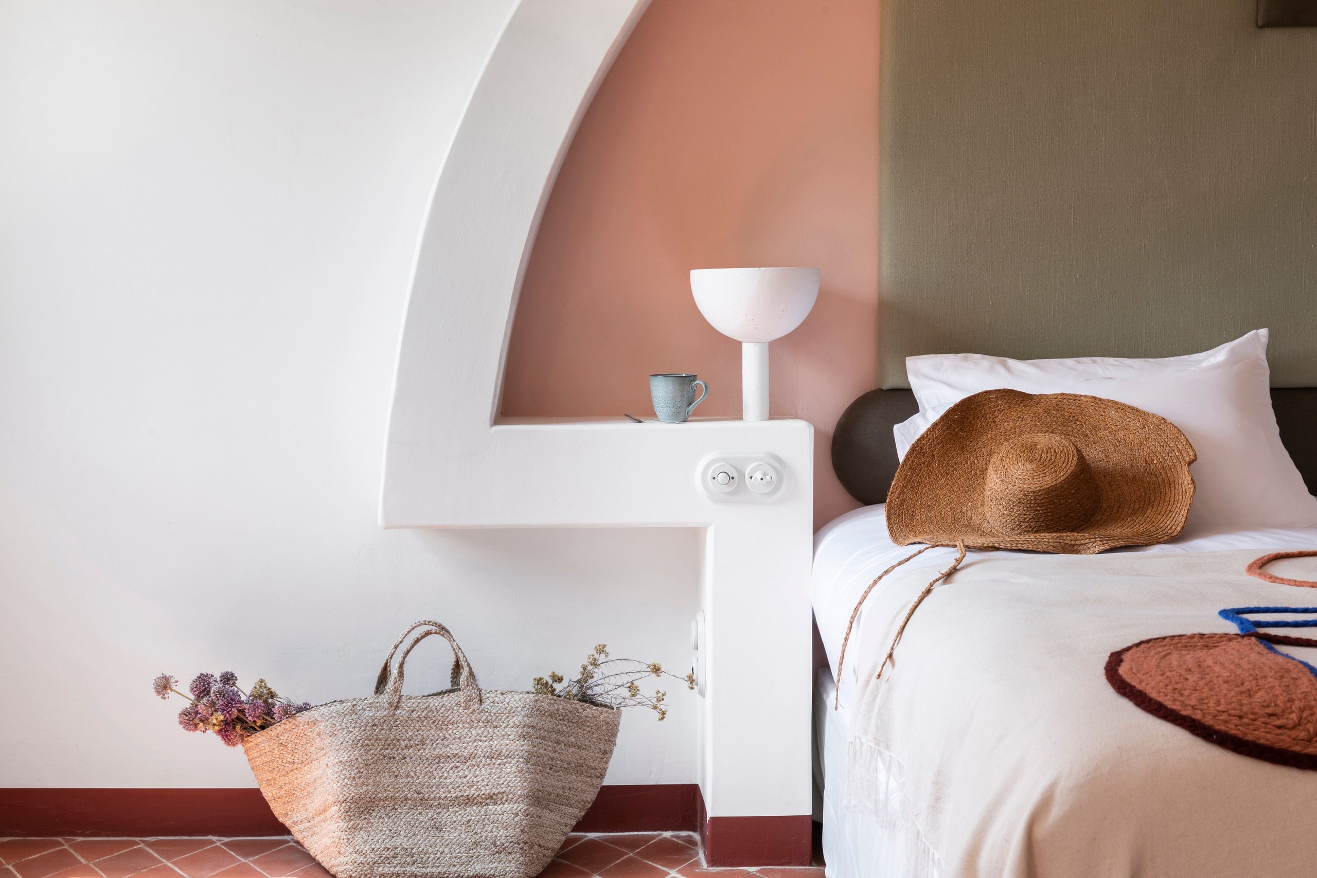 Menorca Experimental, Balearic Islands, Spain — Minimalist bedroom with terracotta accent wall, white curved alcove, woven accessories, and natural linen bedding.
