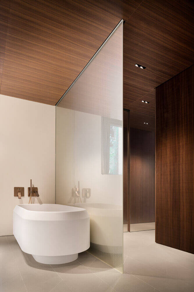 il Sereno Lago di Como, Lake Como, Italy — minimalist bathroom with white soaking tub, warm wood ceiling, frosted glass partition, and bronze fixtures.