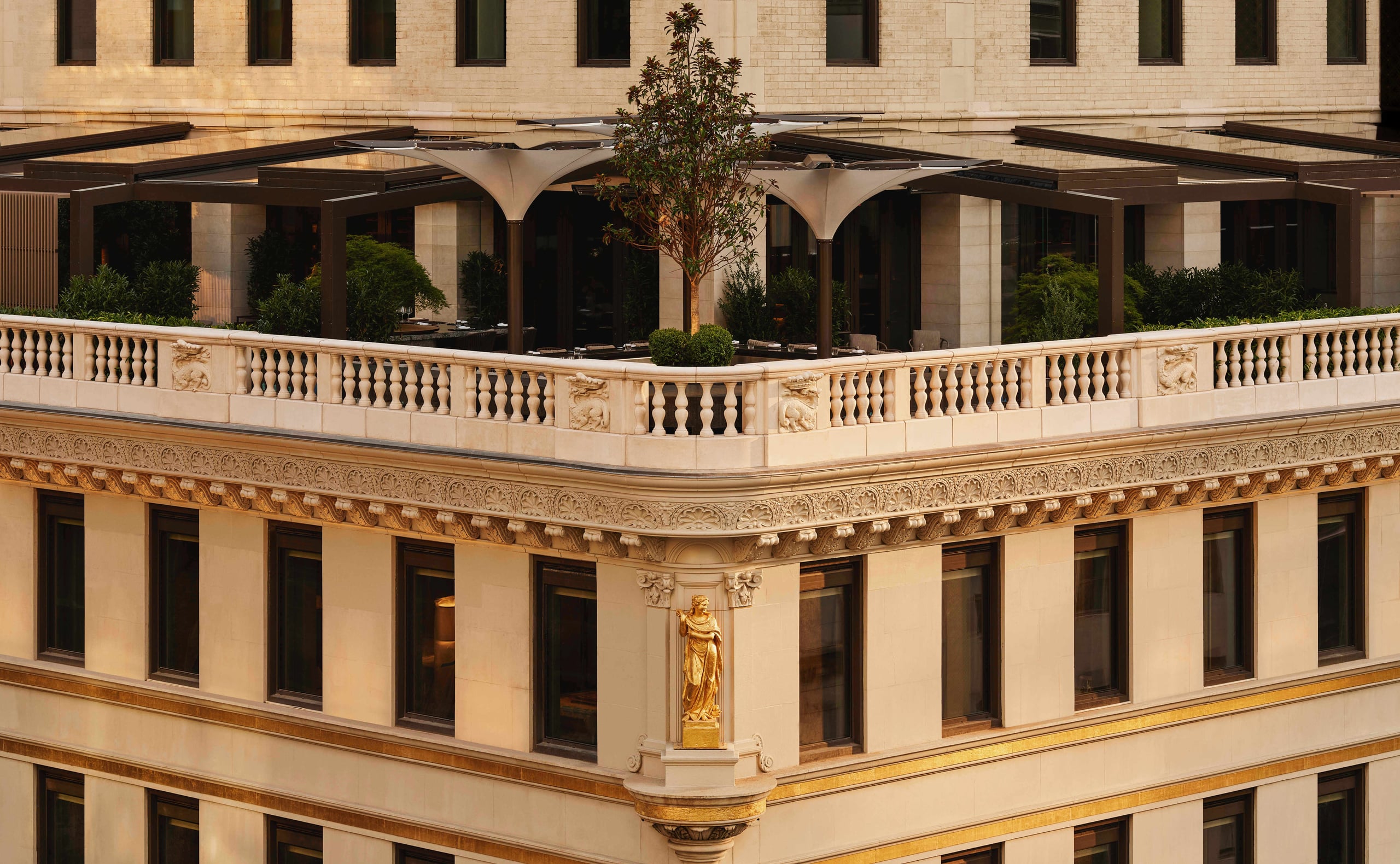 Aman New York, New York, United States — Neoclassical limestone façade with ornamental balustrade, arched pergola, and gilded sculptural details overlooking contemporary courtyard garden.