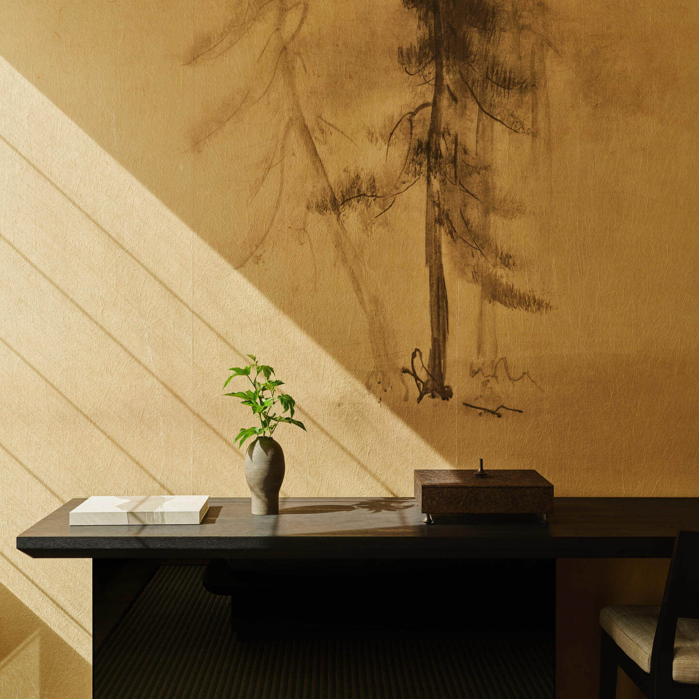 Aman New York, North America — Minimalist desk with potted plant and candle beside ochre wall with tree branch shadow, natural light.