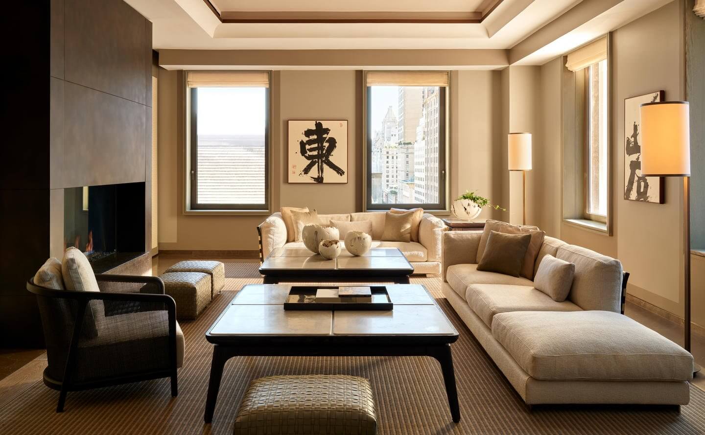 Aman New York, New York, United States — Cream-toned living room with floor-to-ceiling windows, black furniture, cream seating, coffered ceiling, and city views.