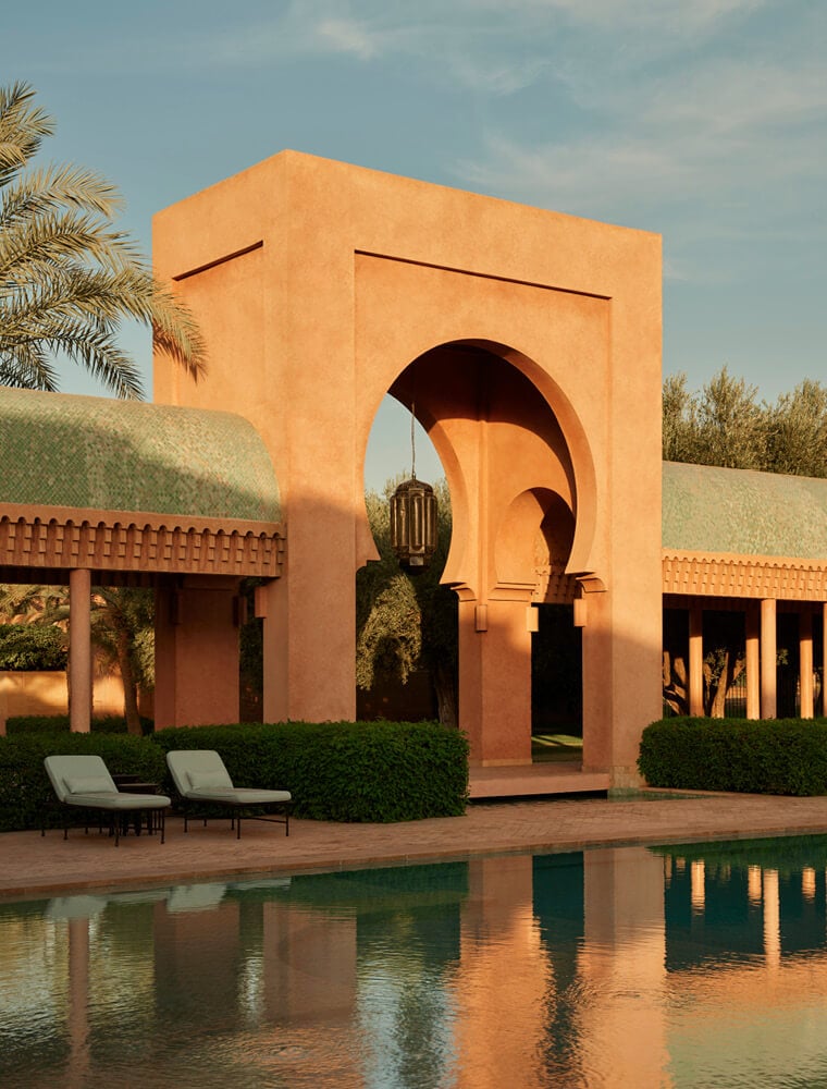 Amanjena, Africa — Terracotta arched gateway with nested horseshoe openings reflecting in still pool, flanked by symmetrical pavilions and manicured hedges.