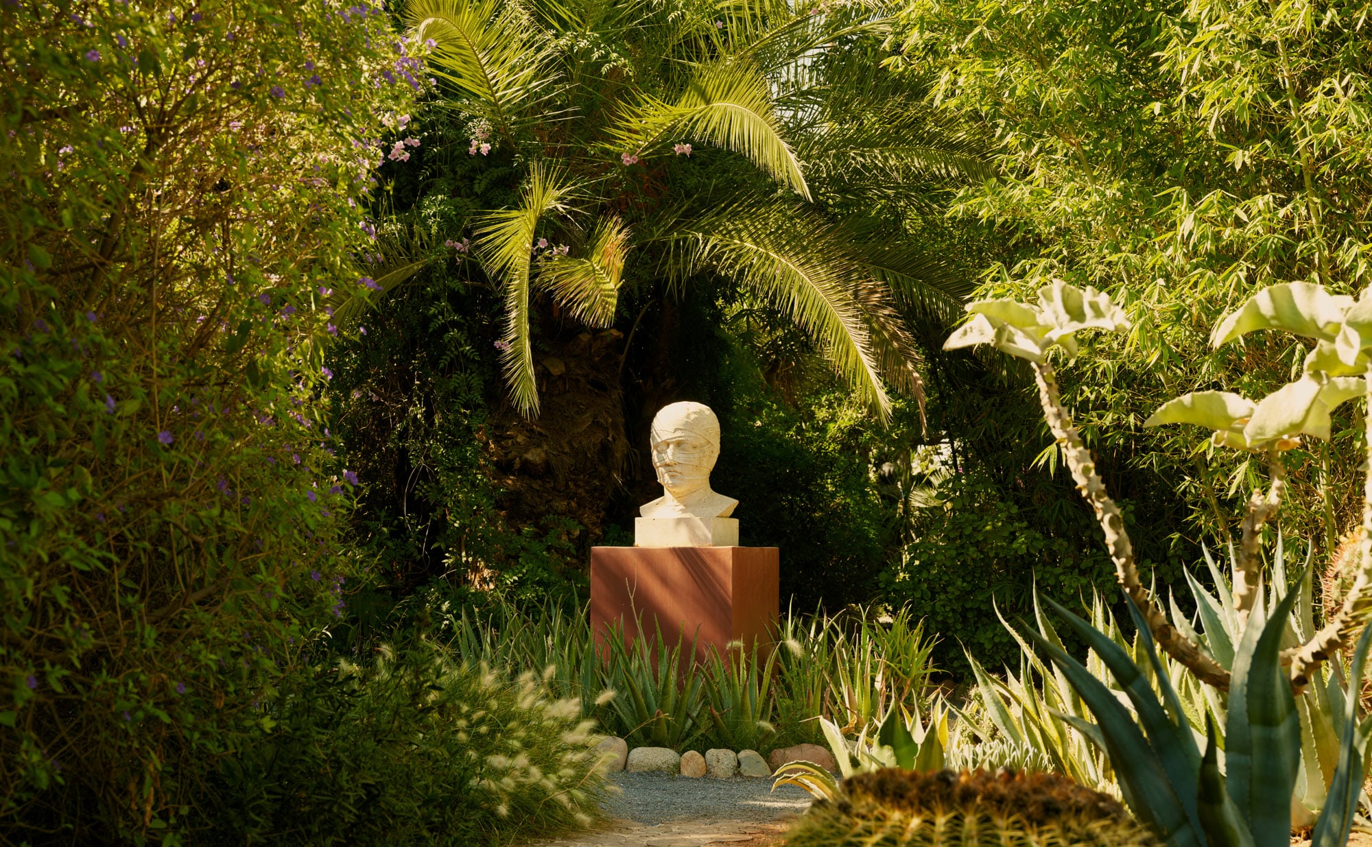 Amanjena, Africa — White marble bust on terracotta plinth framed by lush tropical gardens with palm fronds and flowering vines.