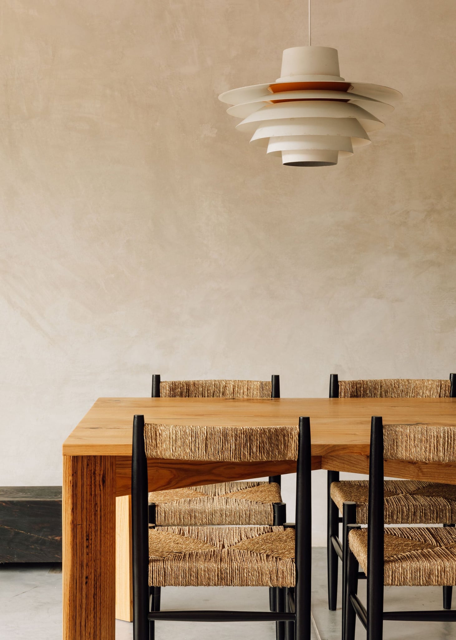 Azores Wine Company, Europe — Minimalist dining space with wooden table, woven-seat chairs, layered pendant lamp, neutral plaster walls.