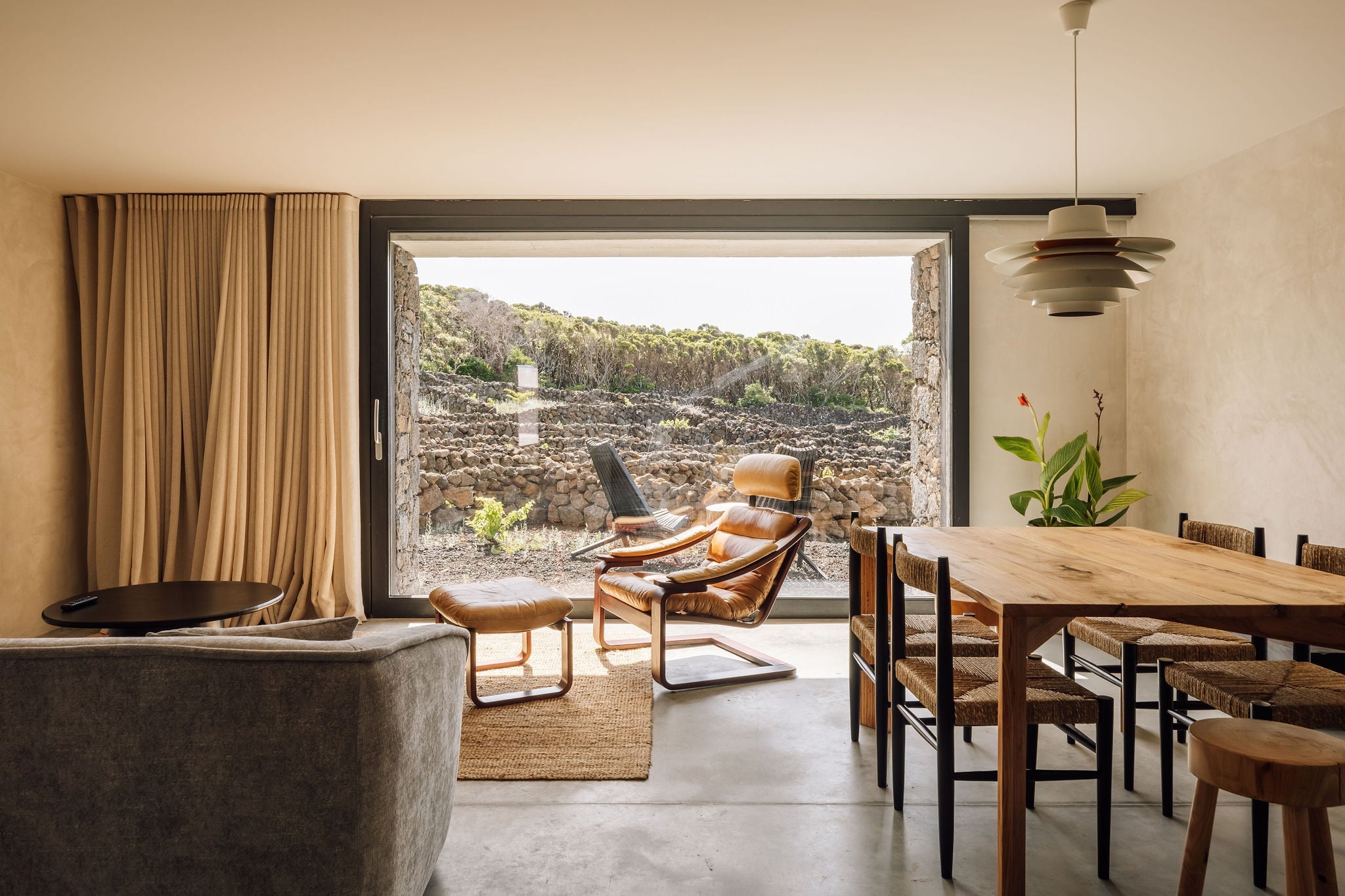 Azores Wine Company, Europe — Modern dining and lounge space with stone terrace, cognac leather chairs, wooden table, and volcanic landscape views.