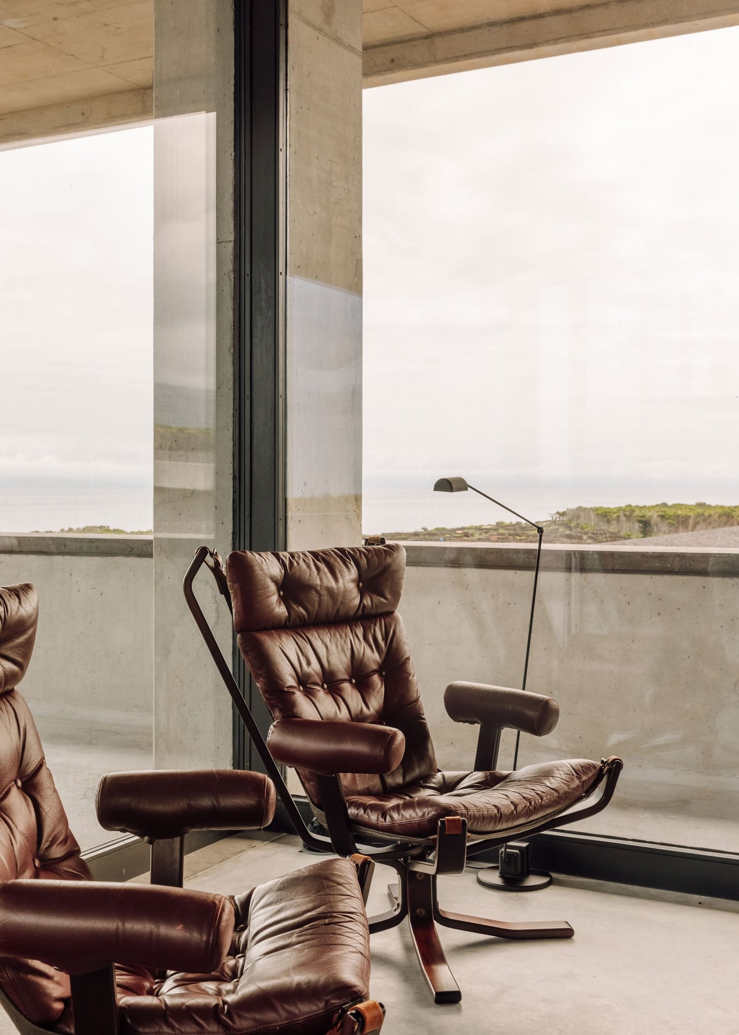 Azores Wine Company, Europe — Cognac leather lounge chairs with ottoman beside floor-to-ceiling windows overlooking coastal landscape and water.