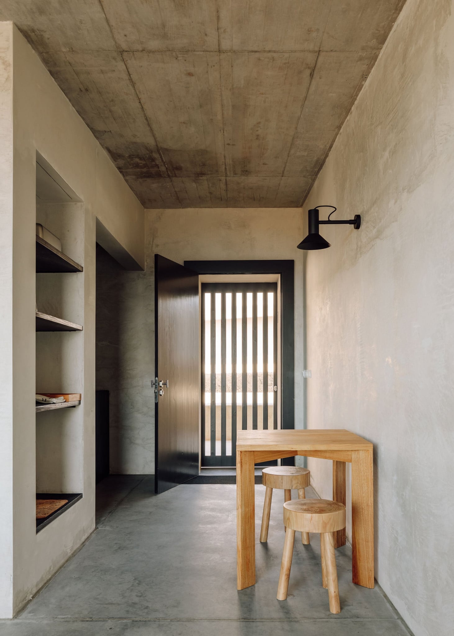 Azores Wine Company, Europe — Concrete ceiling and polished floor with wooden table, built-in shelving, and natural light filtering through vertical-slat door.