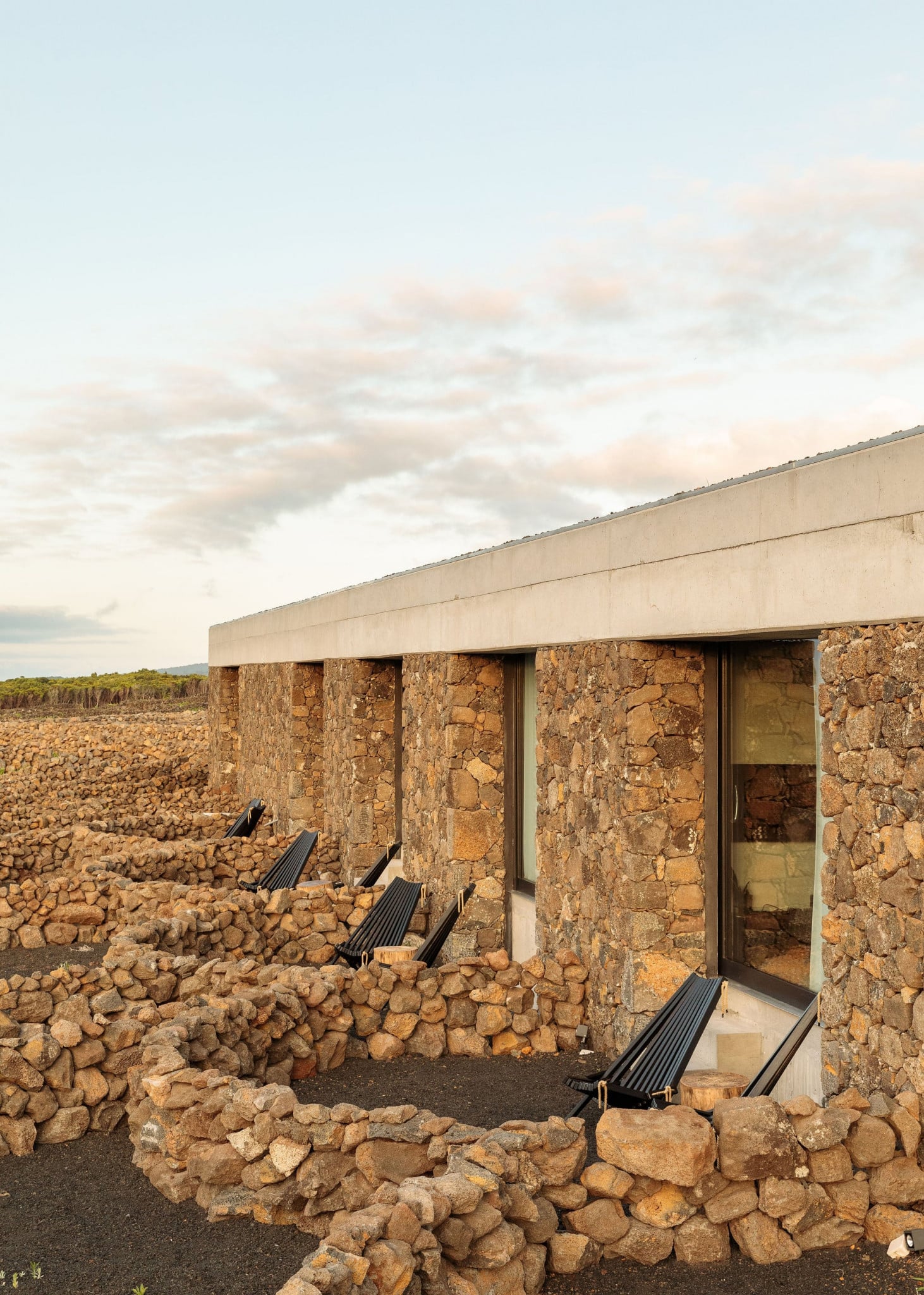 Azores Wine Company, Europe — Stone and concrete pavilion with black lounge chairs overlooking volcanic landscape at dusk.