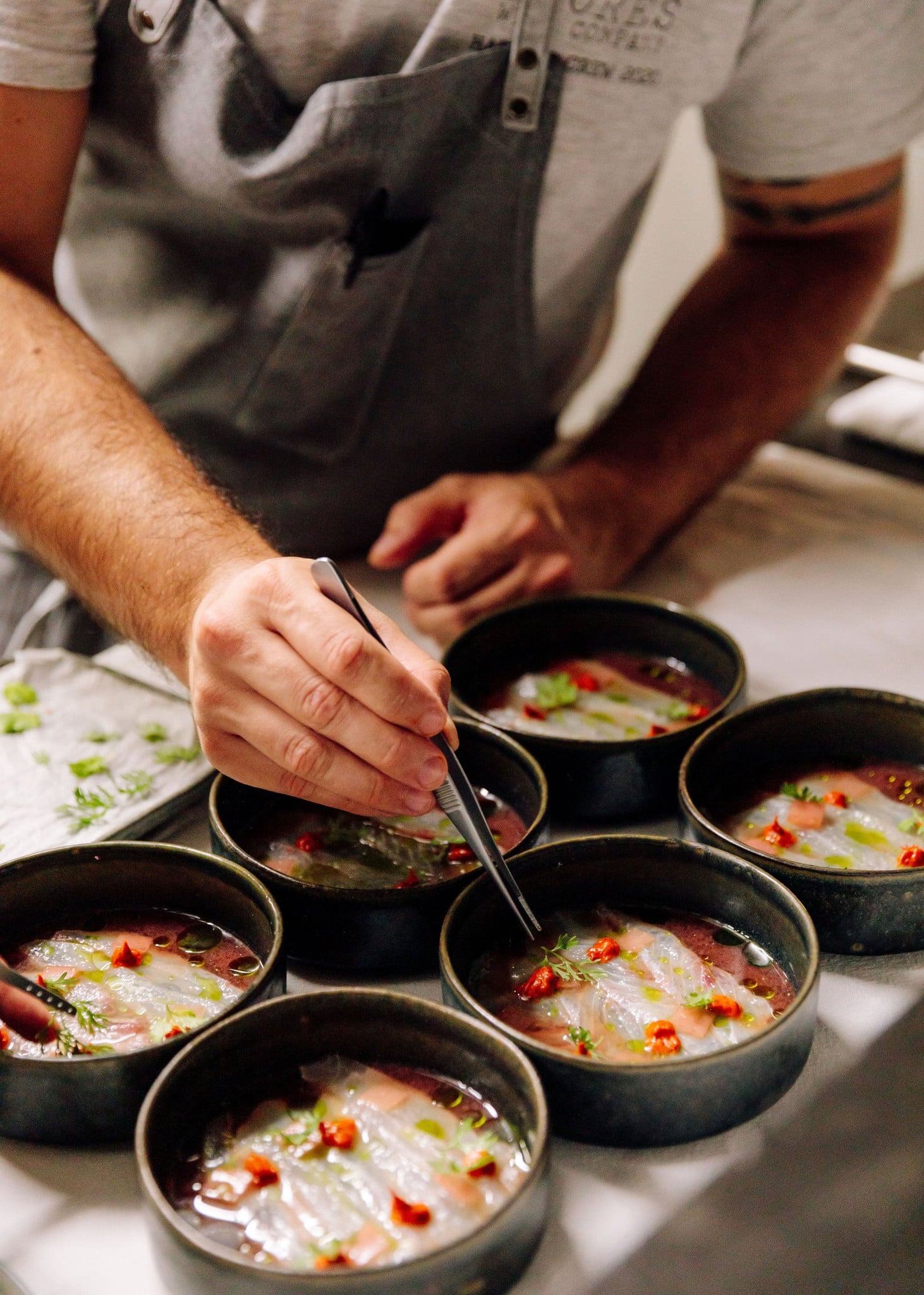 Pico Gastronomy — Chef plating delicate sashimi with microgreens and red chili in black bowls, contemporary fine dining preparation.