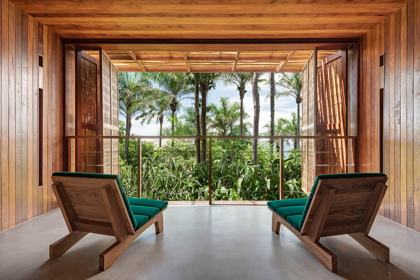 Barracuda Hotel & Villas, South America — Wooden pavilion with teak furniture and emerald cushions overlooking tropical gardens and water beyond open sliding doors.