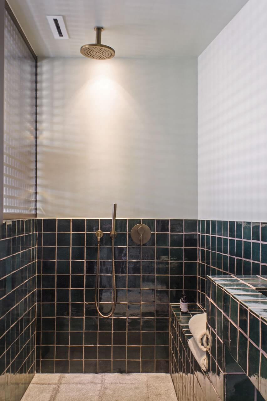 Baja Club, Mexico — Walk-in shower with dark green subway tile, brass fixtures, rainfall showerhead, and soft natural light from skylight above.