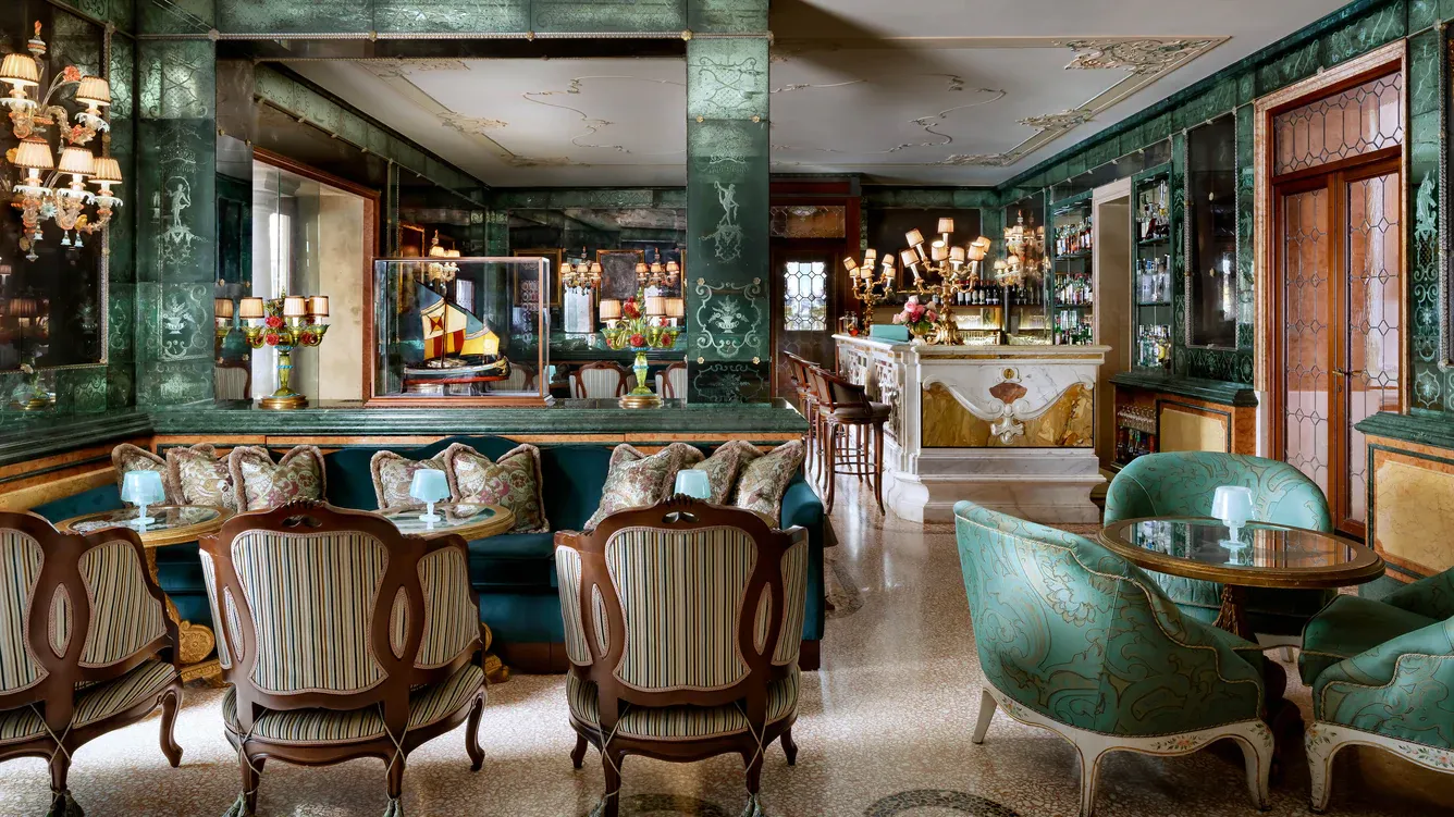 Bar Longhi, Europe — Emerald lacquered walls, brass chandeliers, and striped wood chairs frame an intimate cocktail lounge with marble bar and jewel-toned velvet seating.