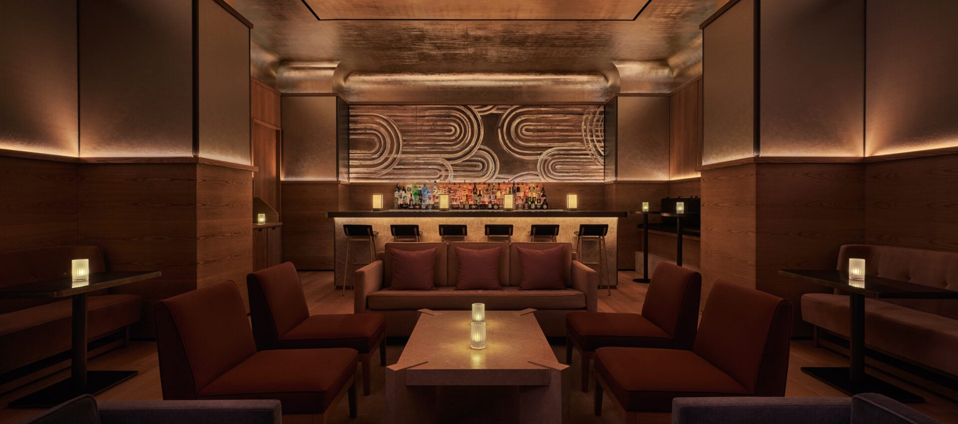 Bar Pendry, North America — Warm wood-paneled lounge with geometric wall art, cognac leather seating, illuminated bar, and ambient lighting creating intimate luxury hospitality space.