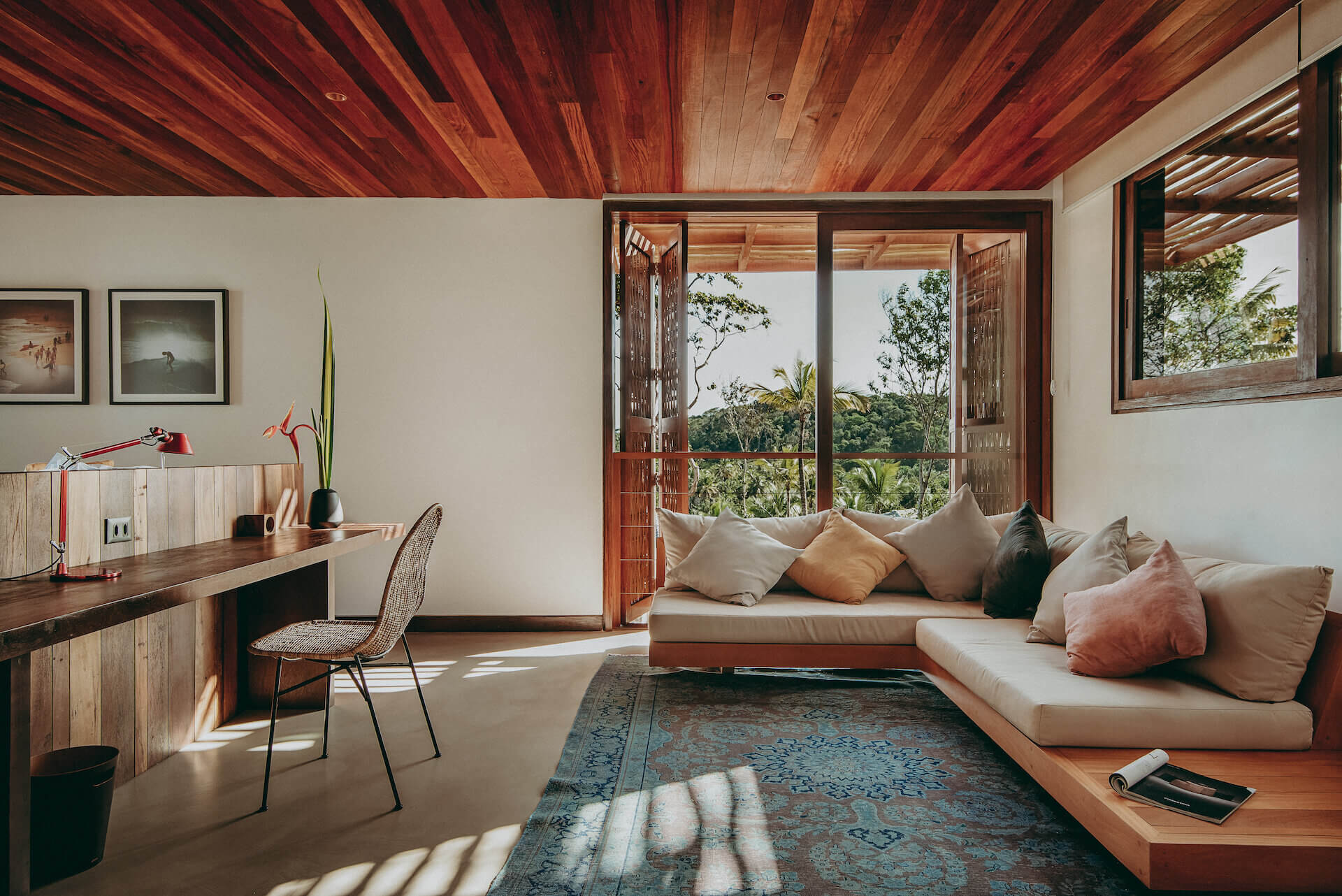 Barracuda Hotel & Villas, South America — Bedroom with timber ceiling, workspace desk, and low-slung daybed overlooking forested landscape through wooden-framed doors.