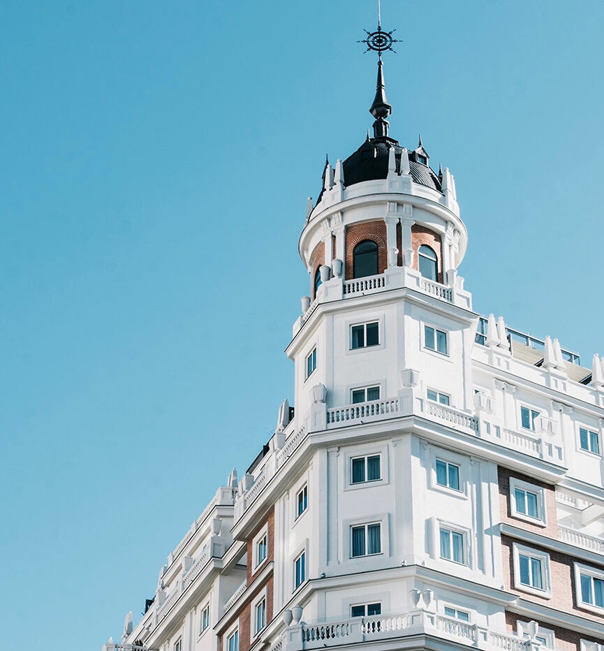 Dear Hotel, Europe — Neoclassical tower with white facade, ornate balustrades, and black cupola against clear blue sky, embodying timeless luxury hospitality design.