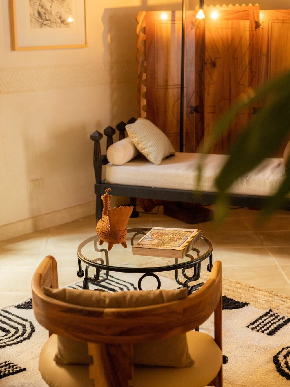 La Valise San Miguel, Mexico — Ochre-toned bedroom with black iron bed, leather chair, round side table, woven accents, warm ambient lighting, and geometric patterned rug.
