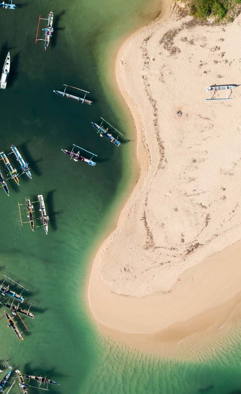 Cap Karoso, Asia — Aerial view of traditional outrigger boats anchored in emerald shallows beside pristine sand beach, soft natural light.