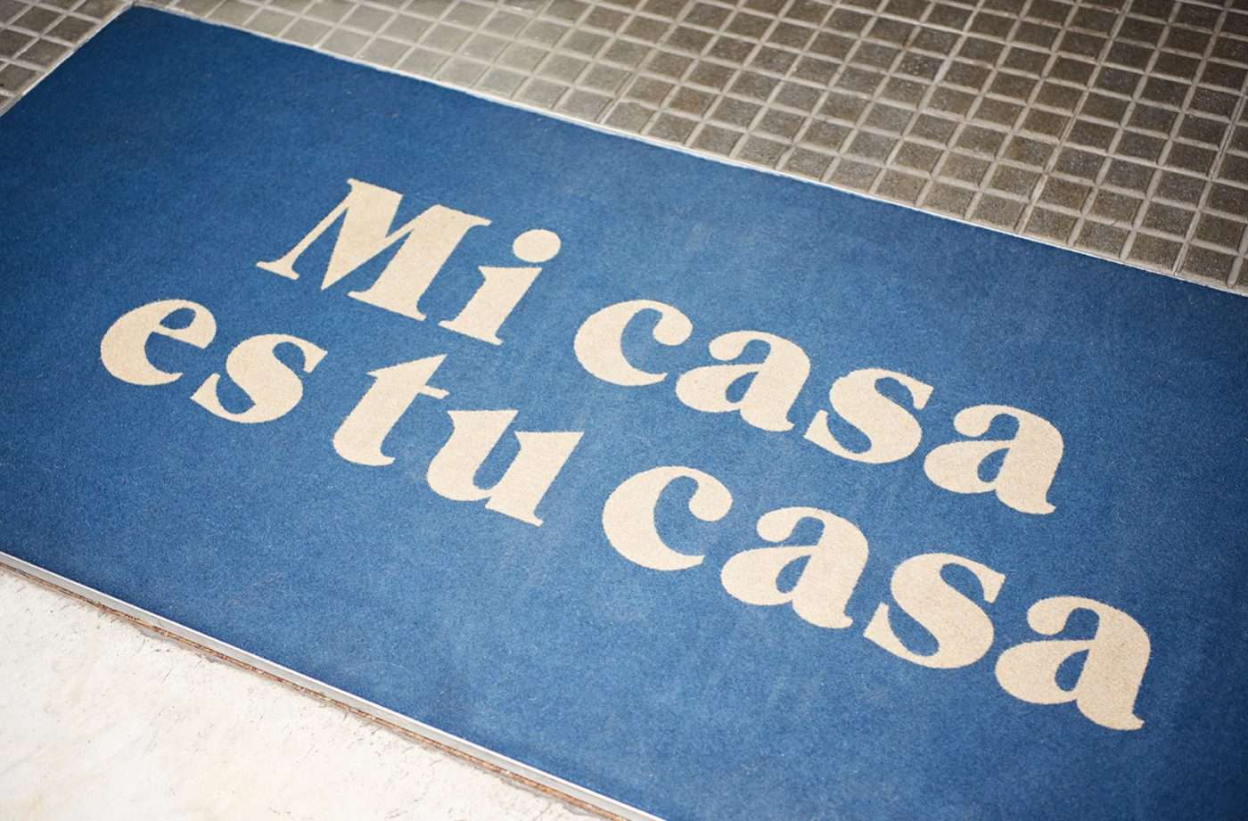 Casa Bonay, Europe — Blue entrance mat with cream serif lettering on tiled floor, luxury hospitality branding detail.