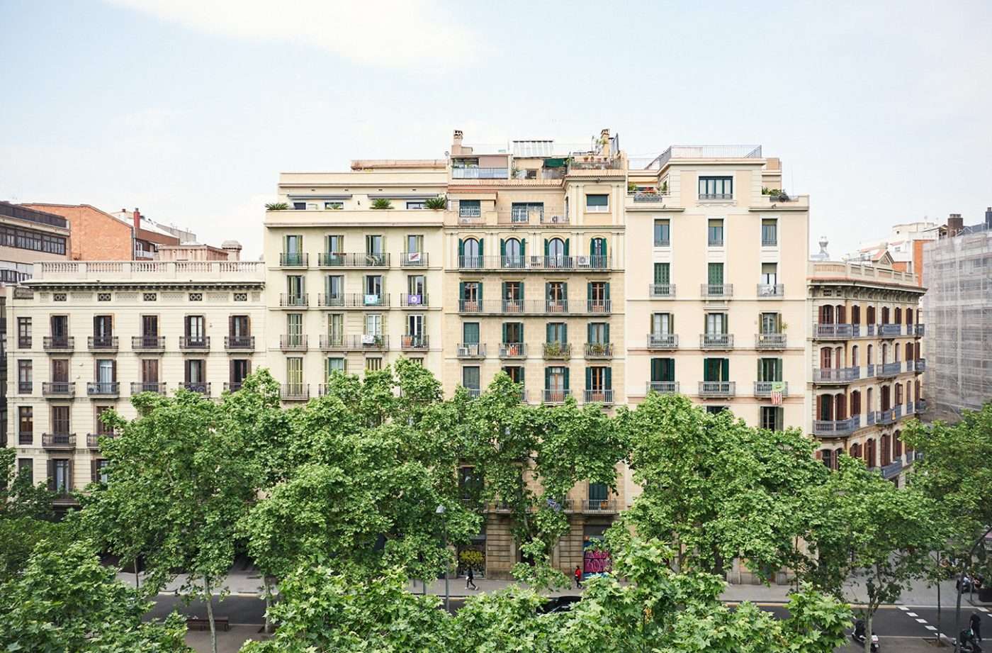Casa Bonay, Barcelona, Spain — Cream-colored Eixample apartment buildings with wrought-iron balconies overlooking verdant plaza trees, afternoon light.