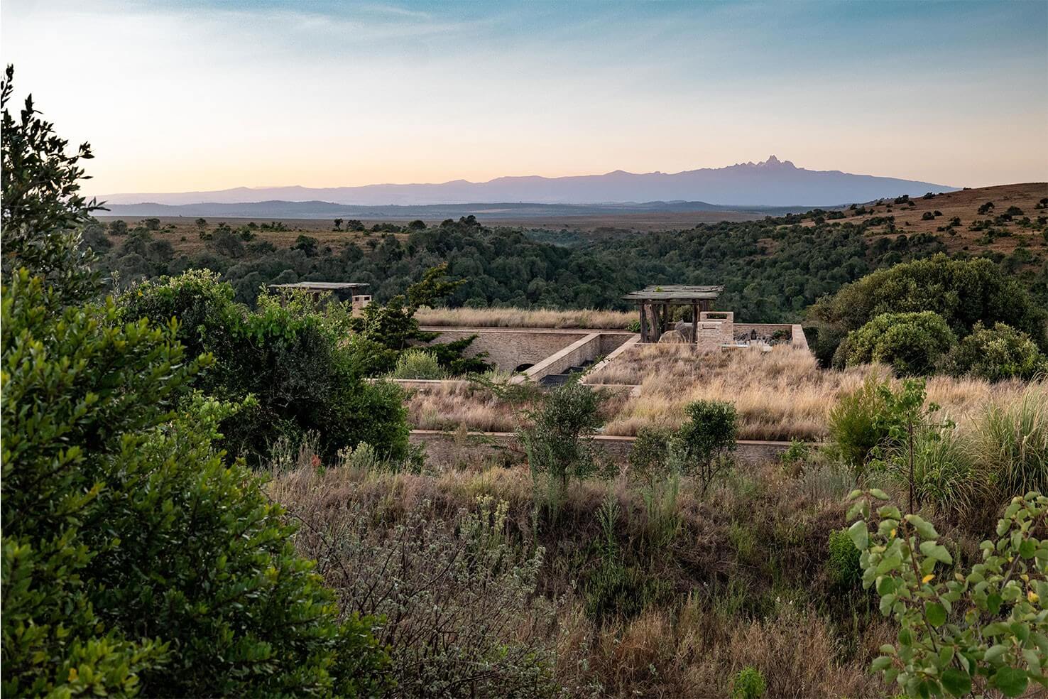 Arijiju Retreat, Africa — Stone pavilion overlooking forested valley with distant volcanic peak at dusk, contemporary architecture nestled in savanna landscape.
