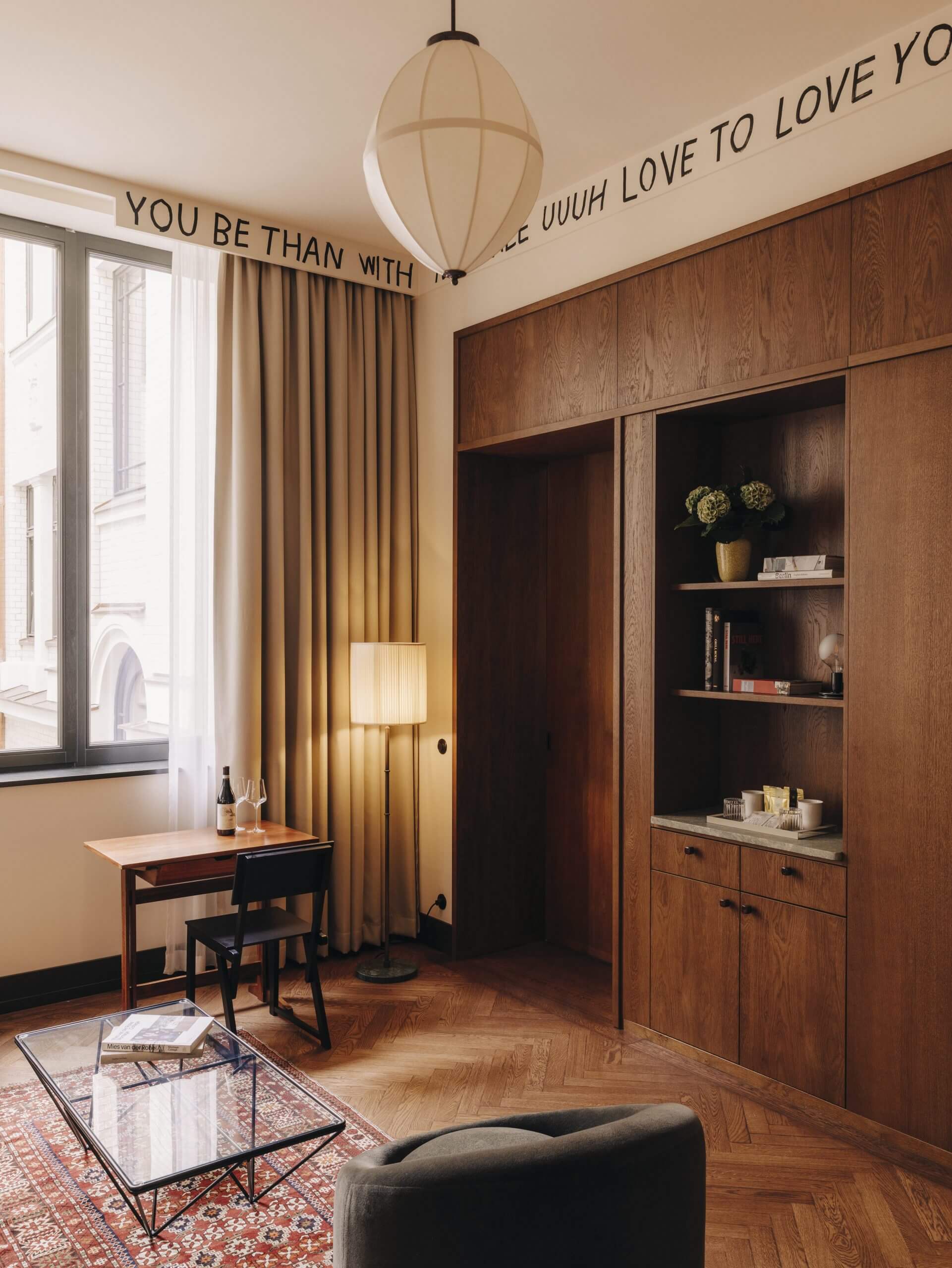 Château Royal, Europe — Mid-century wood-paneled suite with herringbone floors, brass pendant light, and motivational wall text in warm minimalist aesthetic.