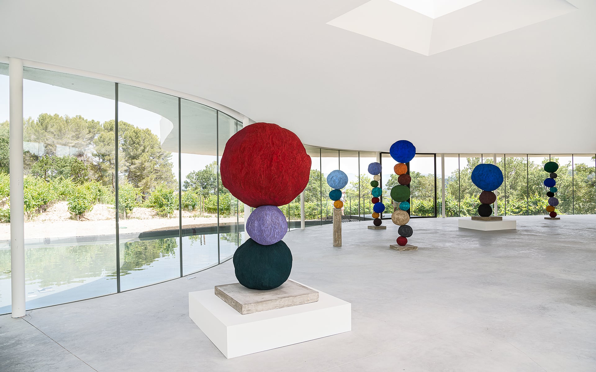 Chateau la Coste, Europe — Minimalist gallery interior with stacked colored spheres, floor-to-ceiling windows, polished concrete floors, skylight, vineyard views.